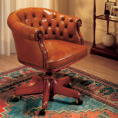 Brown leather presidential armchair with a curved back and buttoned upholstery, mounted on a swivel base with brass casters.