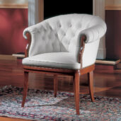 White leather armchair with a curved back and buttoned upholstery, resting on a wooden base with solid wood legs.